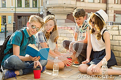 Happy 4 teenage friends or high school students are having fun, talking, reading phone, book. Friendship and people concept, city Stock Photo