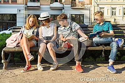 Happy 4 teenage friends or high school students reading books sitting on a bench in the city. Stock Photo