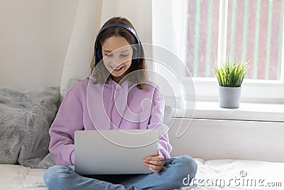 Smiling teenager in headphones using laptop at home Stock Photo