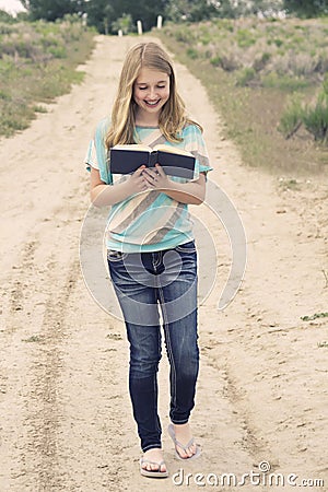 Happy teenage girl reading a book while walking down a dirt road Stock Photo