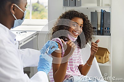 Happy teenage girl showing thumbs up gesture while being immunized against viral infections. Stock Photo