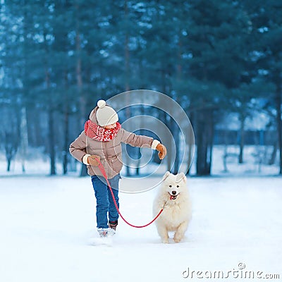 Happy teenager boy running and playing with white Samoyed dog outdoors in the park on a winter day Stock Photo