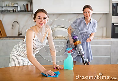 Young girl cleaning the table surface, mother vacuum-cleaning in the kitchen Stock Photo