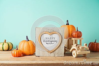 Happy Thanksgiving concept with photo frame, toy truck and pumpkin decor on wooden table over blue background. Autumn season Stock Photo