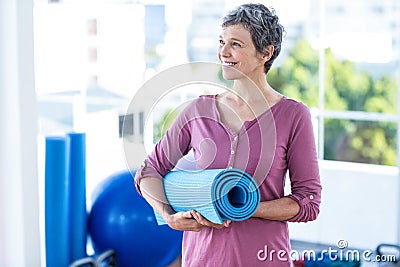 Happy thoughtful mature woman with yoga mat Stock Photo