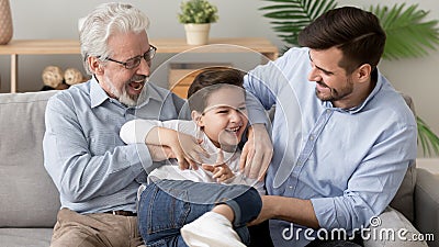 Happy three generation men family playing laughing tickling on sofa Stock Photo