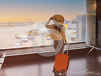 Asian young tourist woman holding the luggage and watching the flight and sunlight through window in Airport terminal Stock Photo