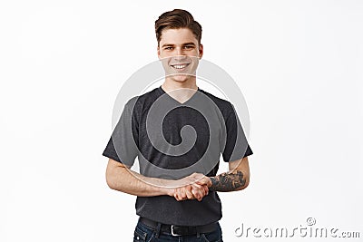 Happy to assist you. Smiling helpful young man holding hands together and looking friendly, listening to customer client Stock Photo