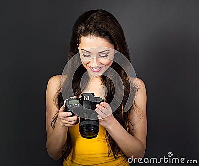 Happy toothy smiling young female photograph looking on the screen of camera and joying the photo on dark grey background Stock Photo
