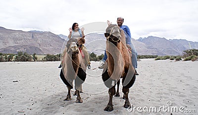 A happy tourist couple riding on double humped Bactrian camels Stock Photo