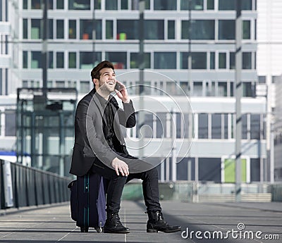 Happy travel man talking on mobile phone while sitting on suitcase Stock Photo