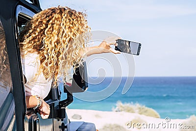 Happy travel woman and enjoy sea beach destination taking smart phone picture from inside her car - free female people drive and Stock Photo