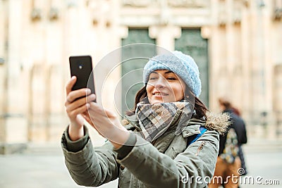 Happy travel woman taking photo with her phone. Autumn or winter trip. Young woman in warm clothes enjoying journey in Europe. Peo Stock Photo