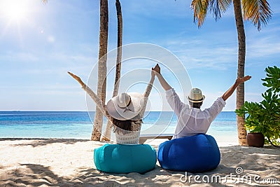 A happy traveler couple sits on bean bags at a tropical beach Stock Photo