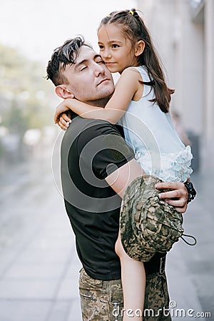 Happy Ukrainian soldier returning from the war meets his little daughter and embraces her Stock Photo