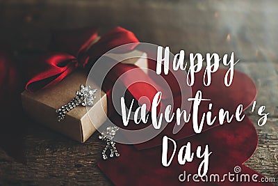 Happy Valentine`s day text on gift box, luxury earrings and red velvet hearts on rustic wood. Card Stock Photo