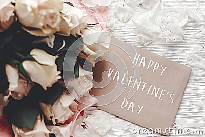 Happy Valentine`s Day text sign on craft greeting card and white roses bouquet on wooden background. Valentines day floral Stock Photo