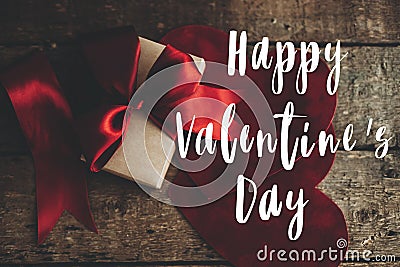 Happy Valentine`s day text on stylish gift box with red ribbon and red velvet hearts on rustic wood Stock Photo