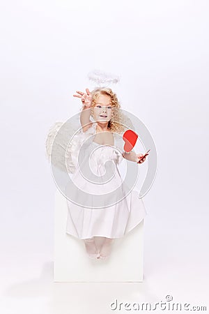 Happy Valentine& x27;s Day. Little baby cupid, beautiful girl in white dress holding paper heart isolated over white Stock Photo