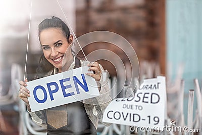 Happy waitress smiles above the open sign as restaurant reopens after corona pandemic Stock Photo