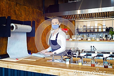 Happy waitress wearing face mask preparing takeaway food behind restaurant counter during Coronavirus lockdown Stock Photo