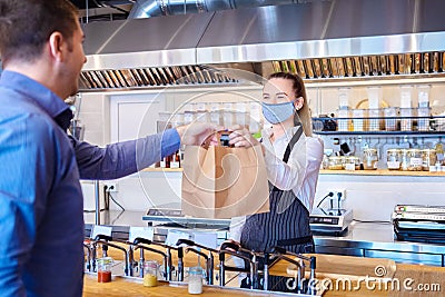 Happy waitress wearing protective face mask serving takeaway food to customer at counter in small family restaurant Stock Photo