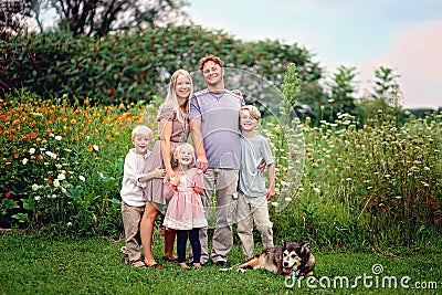 Happy Wholesome Caucasian Family and Dog Smiling and Posing by Flowers Stock Photo