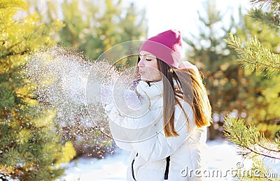 Happy woman blowing on the snow outdoors in sunny winter day Stock Photo