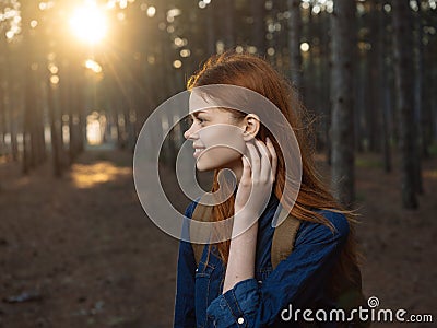 Happy woman in a blue shirt travels in a pine forest and the sunset in the distance Stock Photo