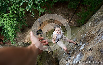 Happy woman climbing rock. Carefree hiker smiling her friend. Man helping his friend to climb rock. Stock Photo