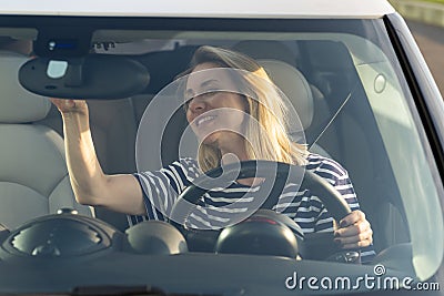 Happy woman drive new car adjust rear view mirror with smile. Adult female vehicle owner first ride Stock Photo