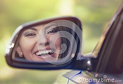 Happy woman driver looking in car side view mirror laughing Stock Photo