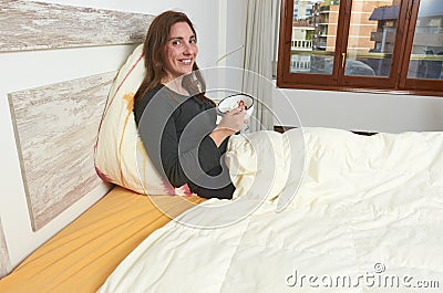 Happy woman eating yogurt with strawberries on bed. Stock Photo