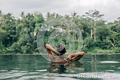 Woman enjoying tropical rain while swimming in infinity pool on Bali Stock Photo