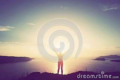 Happy woman with hands up on cliff over sea and islands at sunset Stock Photo