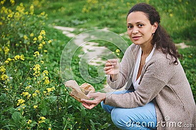 Happy smiling woman looking at camera while picking medicinal herbs in the meadow. Aromatherapy or preparing herbal tea Stock Photo