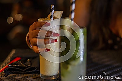 A happy woman holding cold mocktail glass with condensed water droplet during the evening in a restaurant warm weather in Bali Stock Photo