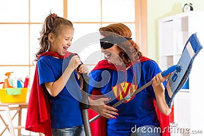 Happy woman and kid prepare for room cleaning. Mother and her child girl playing together. Family in Superhero costumes. Stock Photo