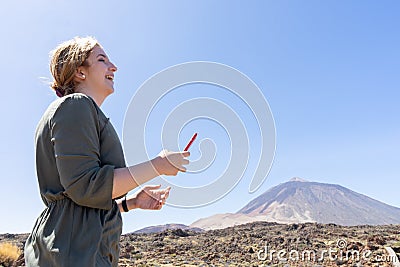 Happy woman laughing, reading a message from social media in her smart phone in a desert spot in the famous volcano El Teide, in Stock Photo