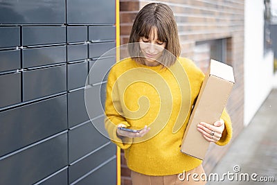 Happy woman with parcel and phone standing near automatic post terminal Stock Photo