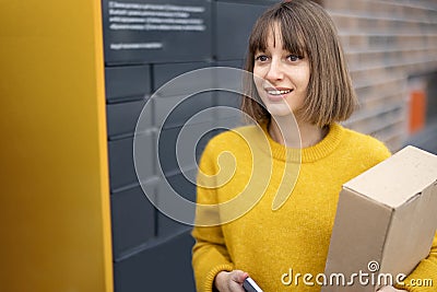 Happy woman with parcel and phone standing near automatic post terminal Stock Photo