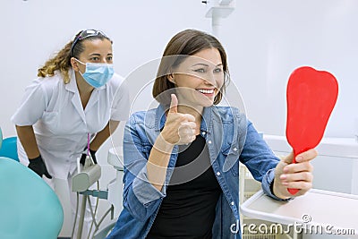 Happy woman patient looking in the mirror at the teeth, sitting in the dental chair Stock Photo