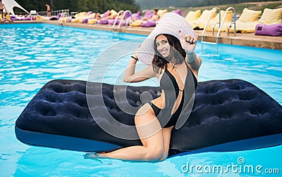 Happy woman with perfect figure sitting on a mattress in the swimming pool and showing thumbs up gesture of good class Stock Photo