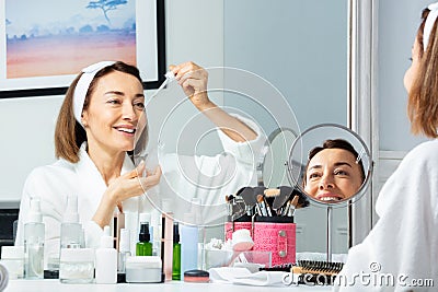 Happy woman putting facial serum with eyedropper on the face Stock Photo