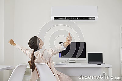 Happy woman relaxing at her office desk under cool, fresh air flowing from the air conditioner Stock Photo