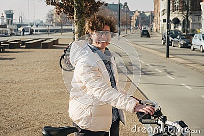 Happy woman renting bicycle at public urban cycle transport station in Copenhagen, Denmark. Young woman taking a shared bicycle. Stock Photo