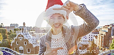 Happy woman in Santa hat at Guell Park with hands framing Stock Photo