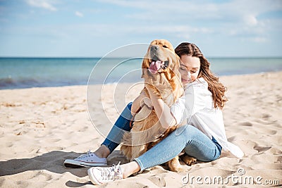 Happy woman sitting and hugging her dog on the beach Stock Photo