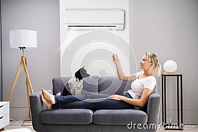 Happy Woman Sitting On Sofa Using Air Conditioner Stock Photo