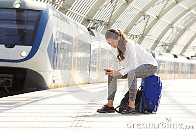 Happy woman sitting on suitcase using mobile phone Stock Photo